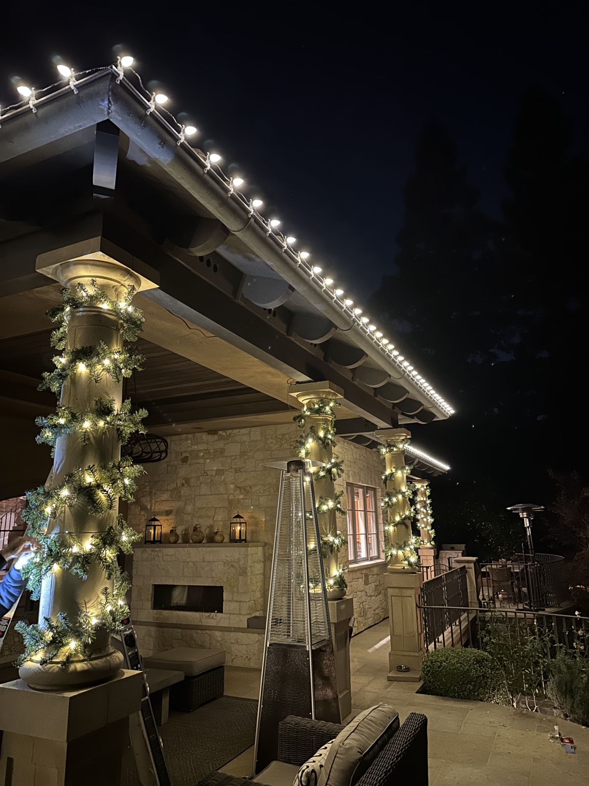 Close-up of professionally clipped warm white C9 bulbs along a gutter with lit garland-wrapped columns