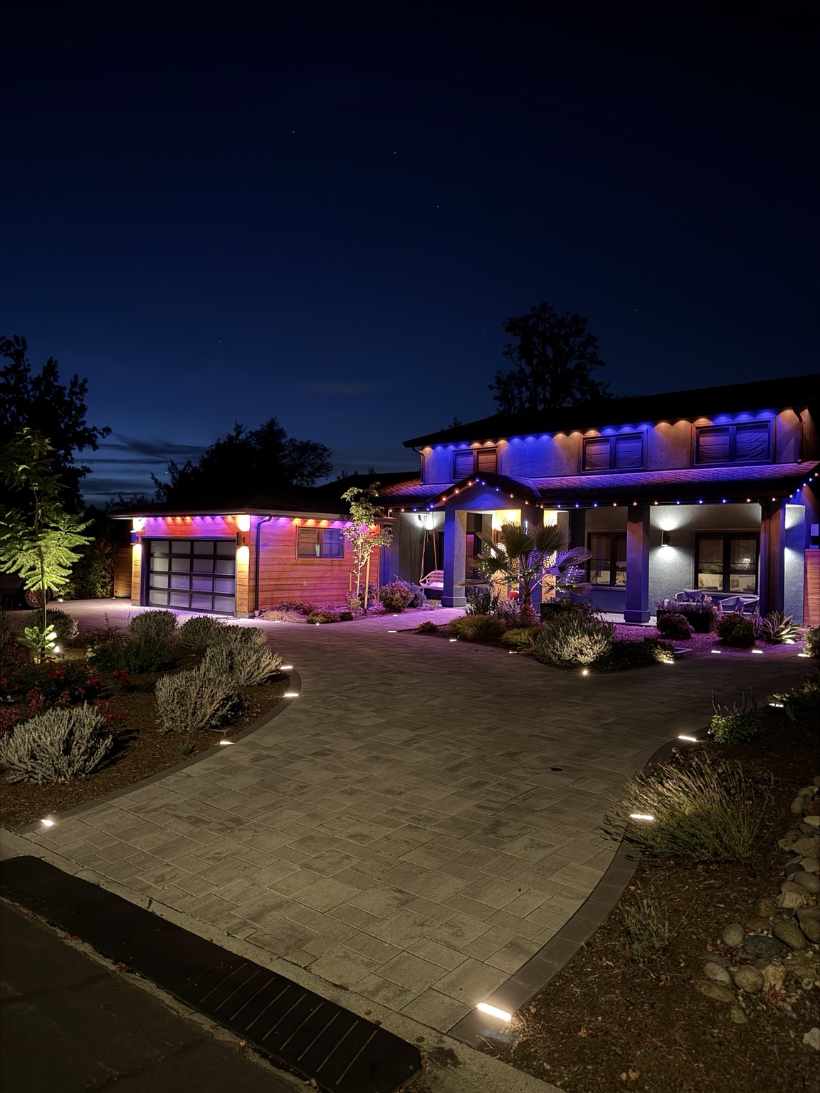 Two-story Bay Area home lit in purple and orange permanent lighting with landscape lighting
